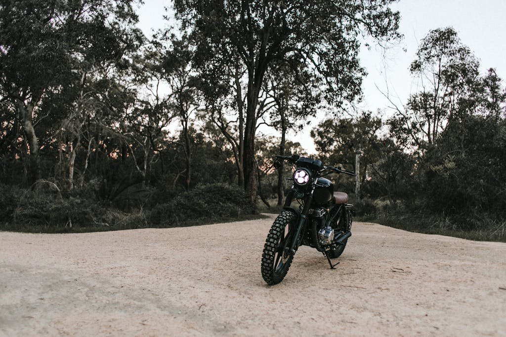 Motorbike parked on sandy ground near trees and plants under blue cloudless sky in summer sunny day